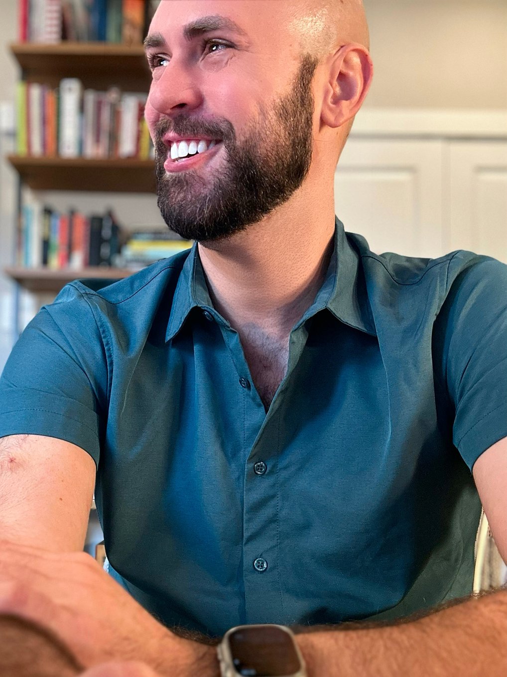 Picture of Cliff in an aqua shirt smiling while sitting in front of a blurred bookcase in his office. 